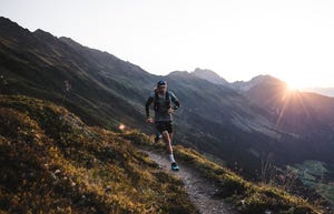 a man running on a trail in a valley with mountains in the background