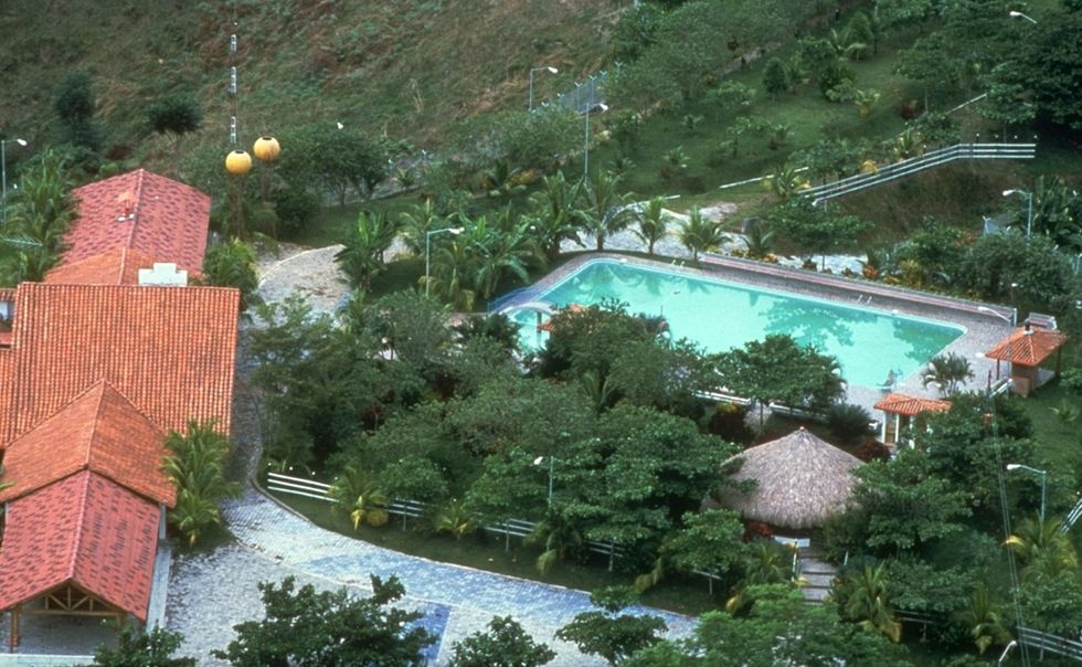 an overhead partial view of a large home and part of its yard that includes tropical plants, a large patio, and a large swimming pool