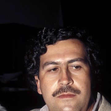 pablo escobar looks away from the camera, he is wearing a sport jacket and a collared shirt and has his signature large mustache