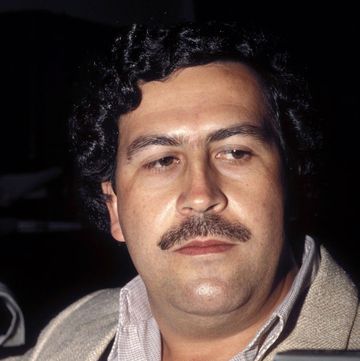 pablo escobar looks away from the camera, he is wearing a sport jacket and a collared shirt and has his signature large mustache