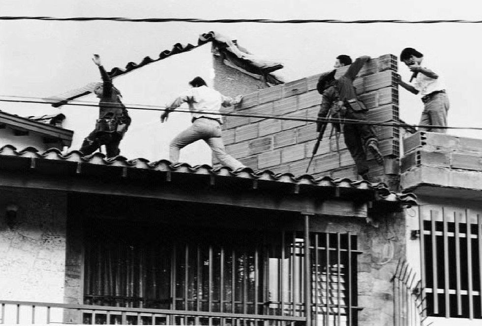 five people run and navigate rooftop obstacles in the search for drug lord pablo escobar, two are obviously armed