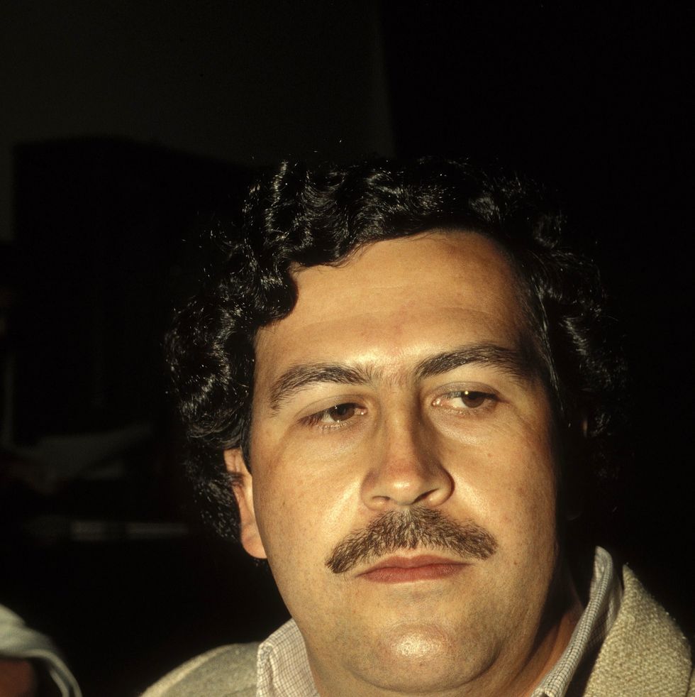 pablo escobar, wearing a tan suit and shit, unsmiling and looking off camera