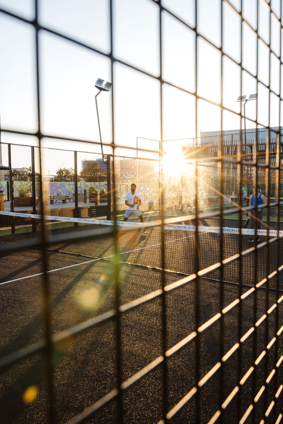 outdoor padel court during sunset with players and a surrounding fence