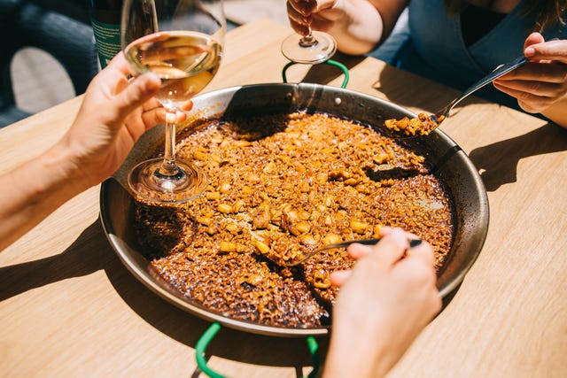 dos personas compartiendo una paella con copas de vino blanco, primer plano de una paella