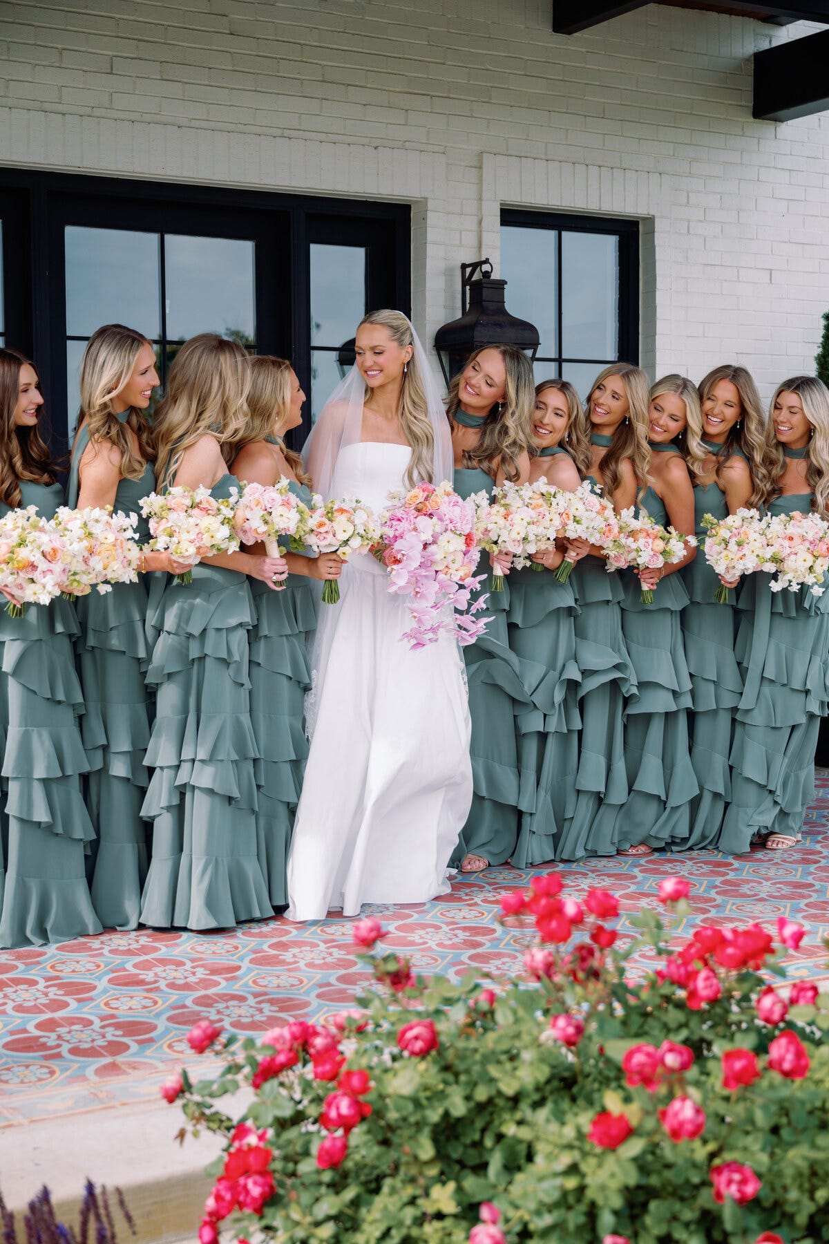 a bride accompanied by bridesmaids wearing matching dresses all holding bouquets of flowers