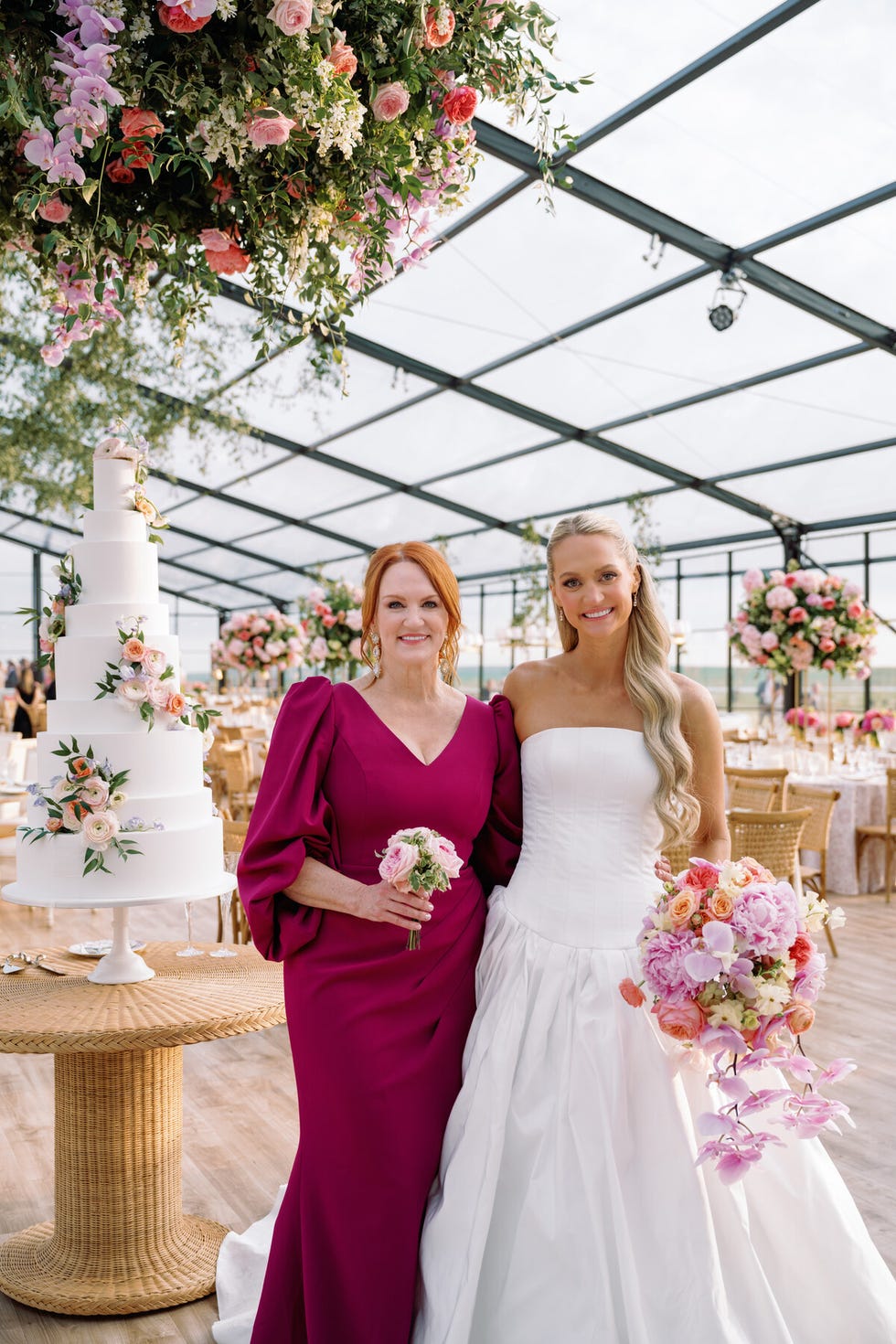 a celebratory scene featuring two women holding bouquets with a cake and floral decorations in the background