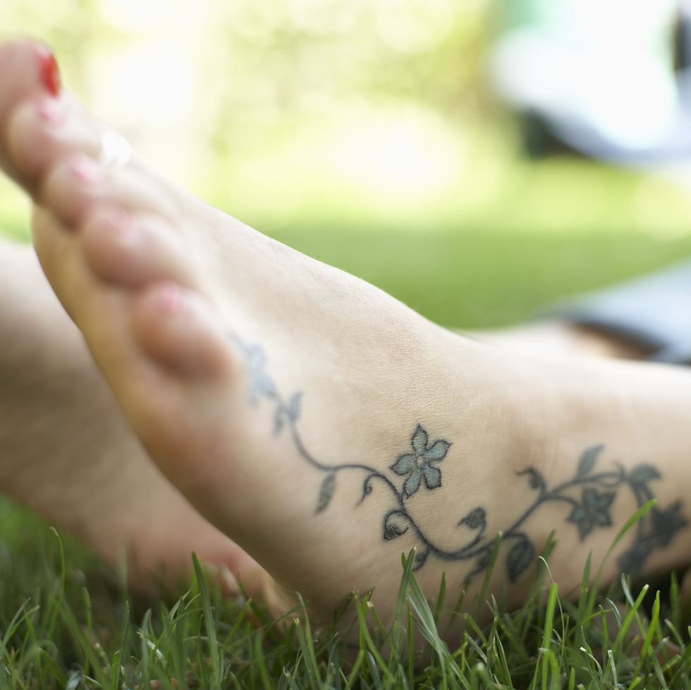 feet resting on grass with flower tattoo over ankle