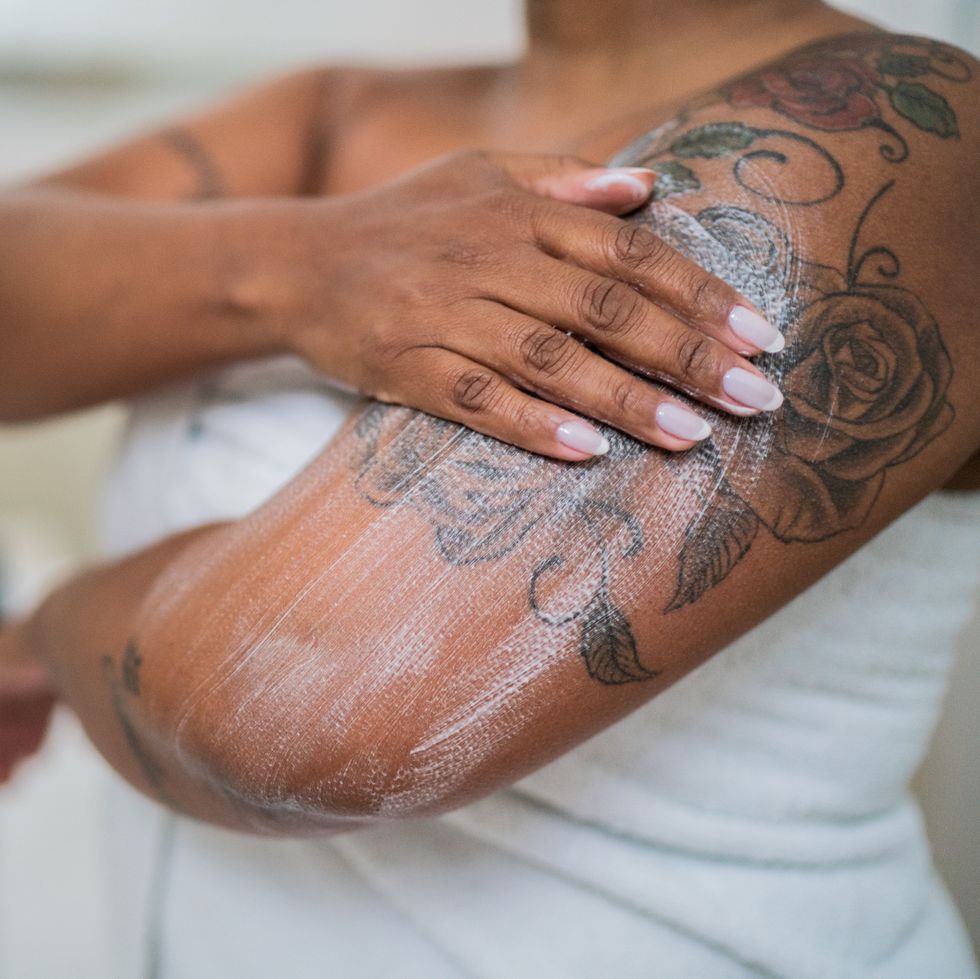 woman applying body lotion over tattoo on arm in the bathroom at home