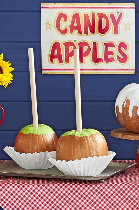 pumpkins painted and decorated to resemble caramel apples on red gingham tablecloth under vintage sign reading caramel apples