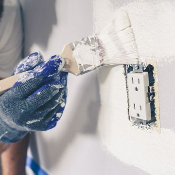 painter man with gloves painting the wall around power outlet