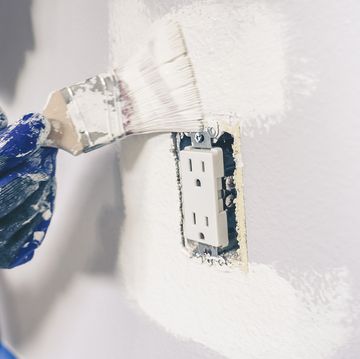 painter man with gloves painting the wall around power outlet