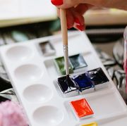 woman dipping paintbrush into paint on palette