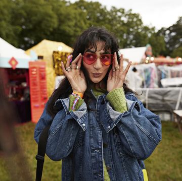 woman puckering and looking away while wearing red sunglasses at market stall during music festival in park