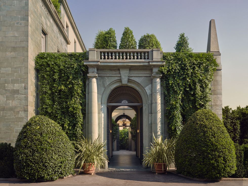 a stone palazzo with a large arched doorway and landscaped trees
