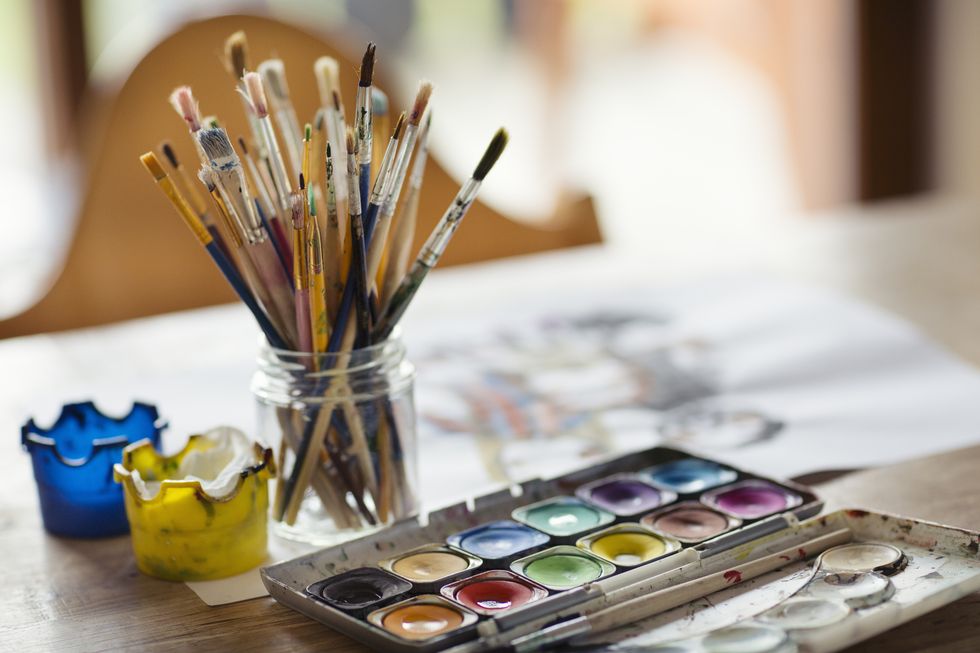 palette of compact paints and a glass jar full of paintbrushes on a dining table
