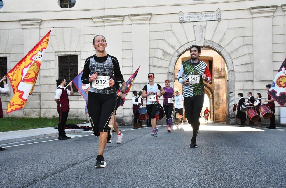 participants running in a race with flags and drummers in the background