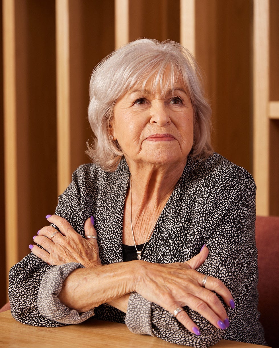 an elderly woman with crossed arms wearing a patterned sweater