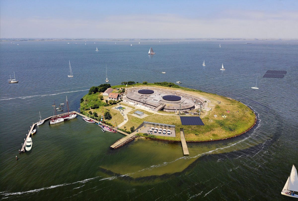 Het nieuwe bezoekers centrum afgebeeld tussen de twee aanlegsteigers zal worden verzonken in de wal van Pampus waardoor bezoekers vanaf het IJmeer weer vrij zicht hebben op de historische geschutskoepels