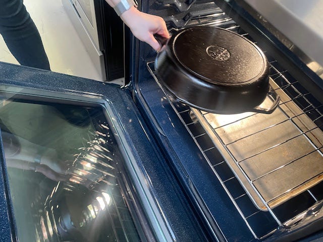 hand placing a cast iron pan into an oven