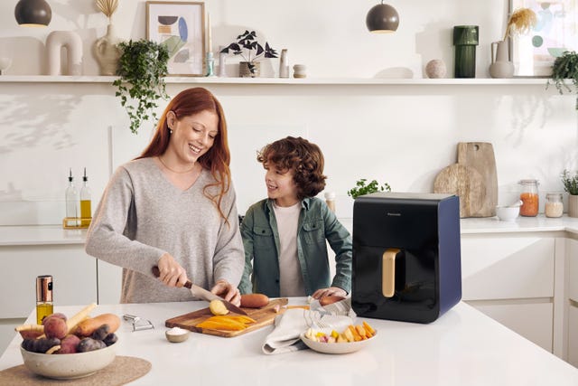 una mujer corta verduras con una airfryer panasonic al lado