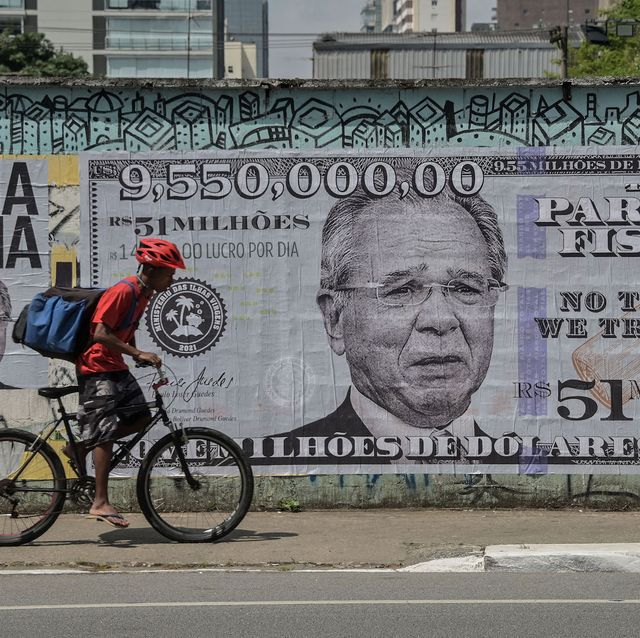 a man rides his bike past a poster depicting brazil's economy minister paulo guedes on a us$955 million bill, in sao paulo, brazil, on october 8, 2021, just days after he was mentioned in the "pandora papers" media investigation exposing world leaders' use of tax havens   according to the investigation, guedes has deposited us$955 million in his offshore dreadnoughts international group, opened in 2014 in the british virgin islands, which was equivalent to r$23 million at the time with the devaluation of the real, accelerated during his tenure at the ministry of economy, the value today corresponds to r$51 million photo by nelson almeida  afp photo by nelson almeidaafp via getty images