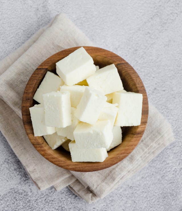 homemade indian paneer cheese made from fresh milk and lemon juice, diced in a wooden bowl on a gray stone background. vertical orientation. top view