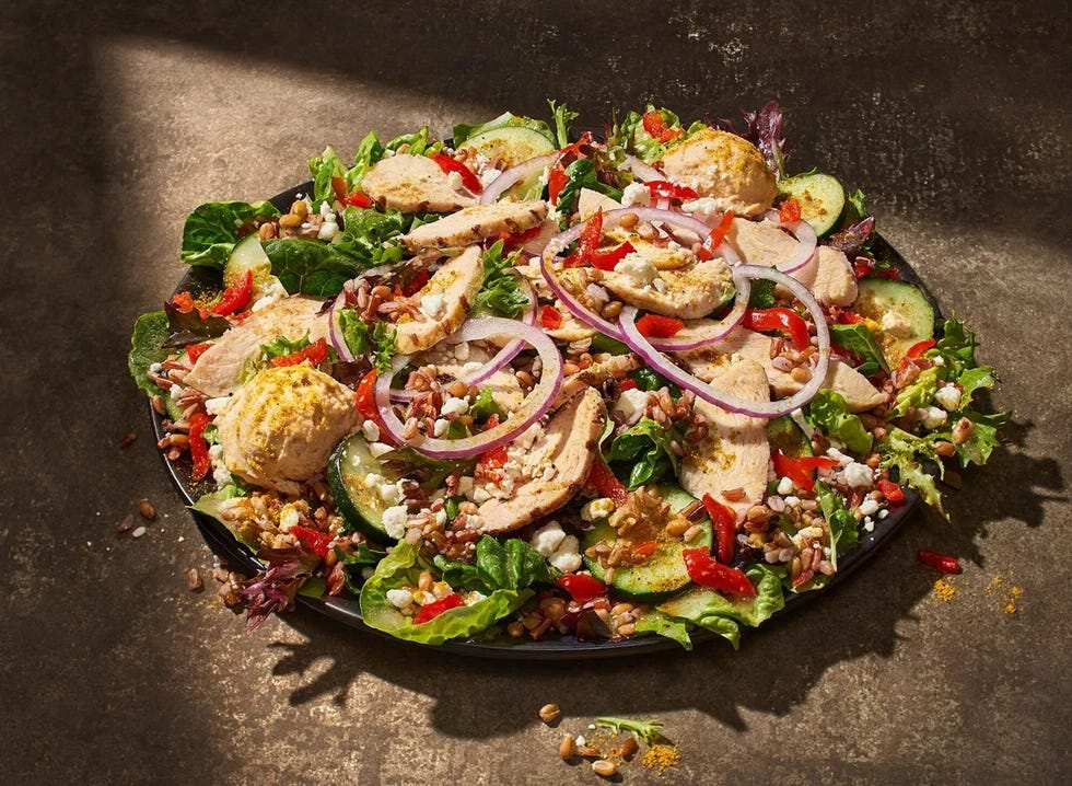 a colorful salad topped with sliced chicken cucumbers and various vegetables