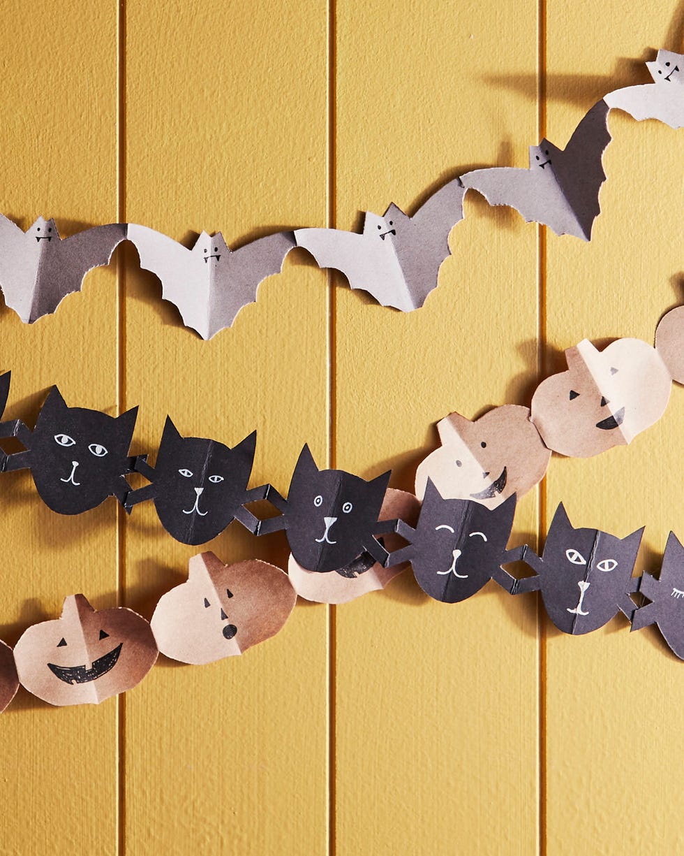 papers chains of bats cut from gray paper cats cut from black paper and pumpkins cut from kraft paper hanging on a yellow slated wall papers chains of bats cut from gray paper cats cut from black paper and pumpkins cut from kraft paper hanging on a yellow slated wall