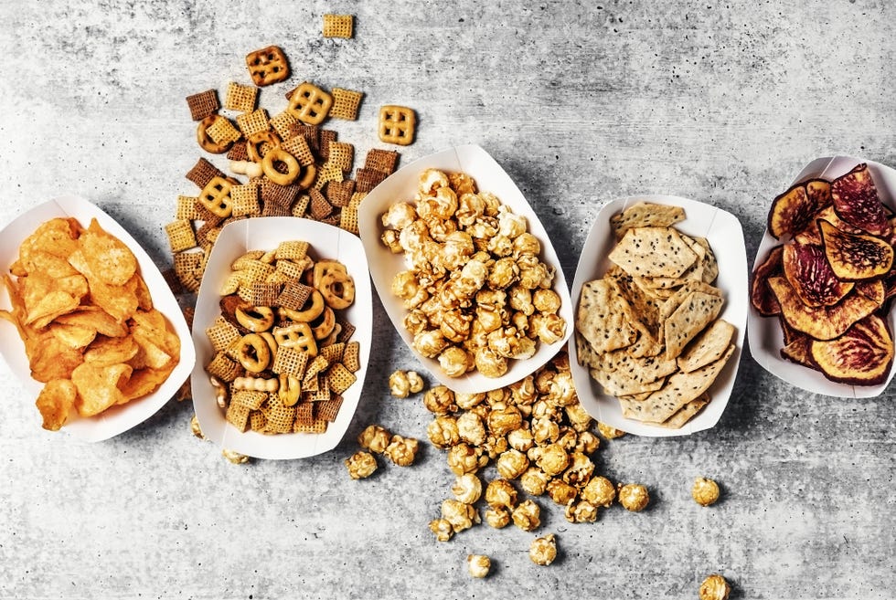 paper trays with caramelized popcorn, chips, and snack mix on gray background