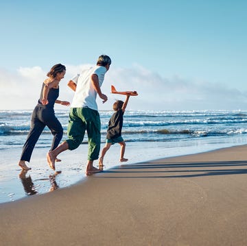 Parents running behind a boy running straight ahead with a model airplane held high in one hand. parents running behind a boy running straight ahead with a model airplane held high in one hand