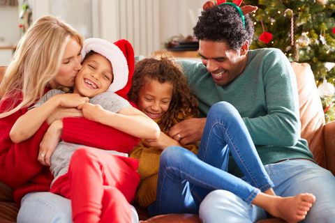 parents tickling children as family sit on sofa celebrating christmas together
