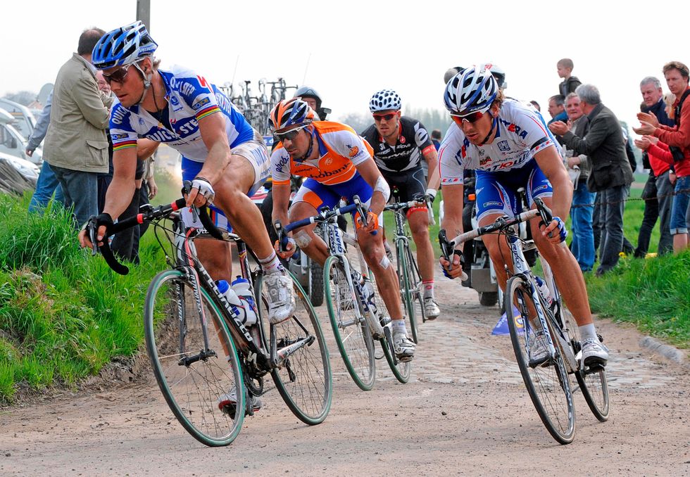 group of cyclists ride on a cobblestone section of the paris roubaix cycling race