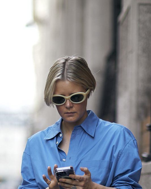 a person in a blue dress and sunglasses holding a phone