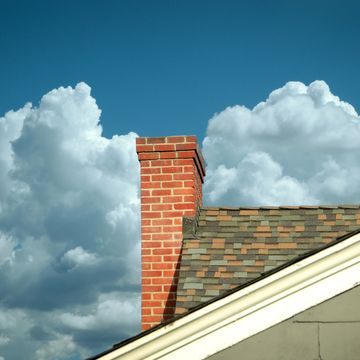 part of tiled roof with brick chimney against clouds
