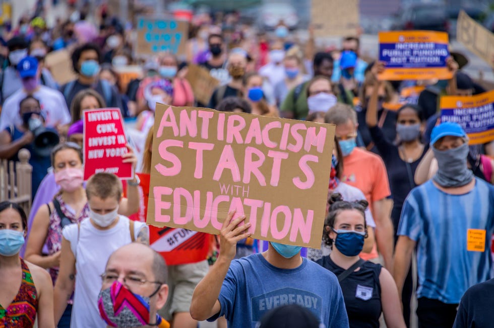 man holding up sign that reads 'antiracism starts with education'