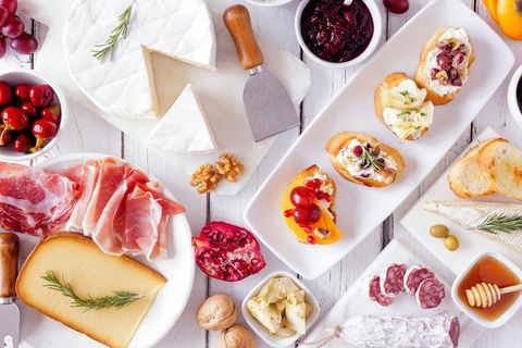 party appetizers of assorted cheeses, meats and crostini, top view on white wood