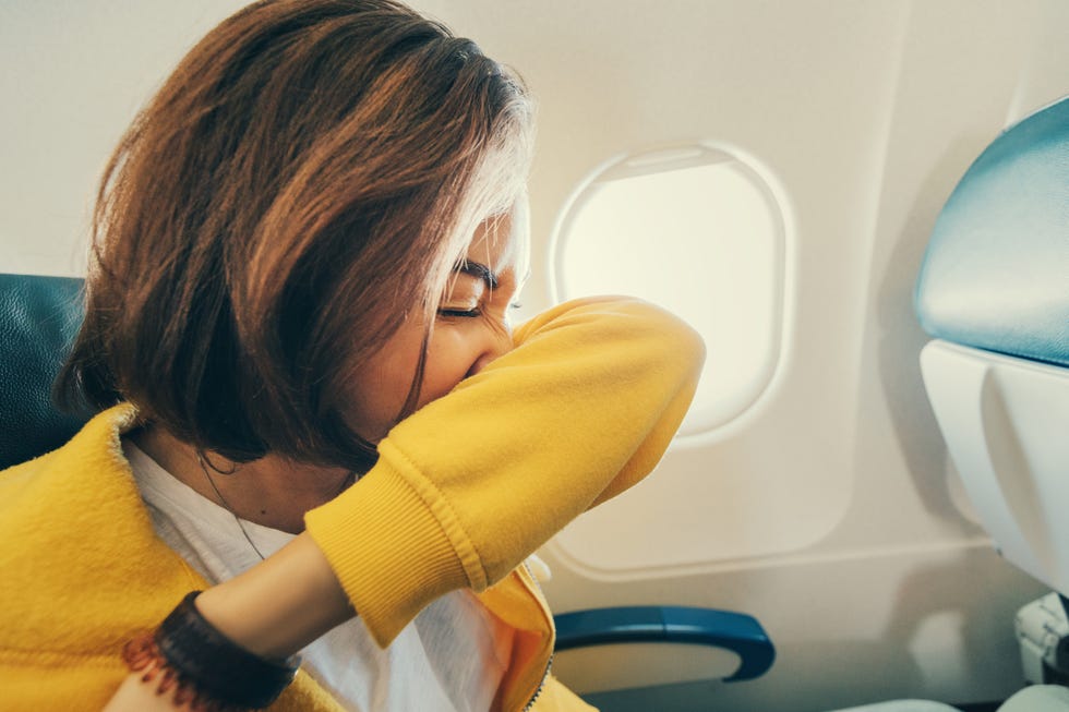 female airplane passenger sneezes into her elbow. first signs of corona virus and covid 19 infection during air transportation
