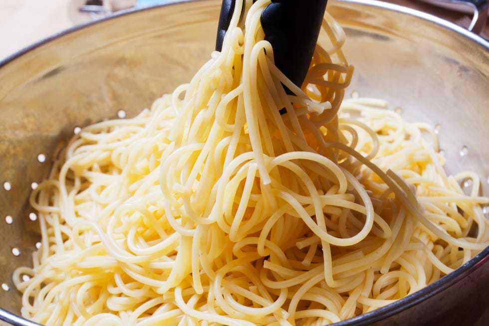 Removing boiled noodles from colander with tongs, close-up
