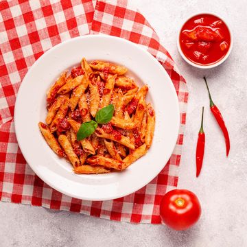 classic italian pasta penne alla arrabiata with fresh basil on a light background, top view