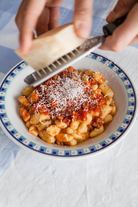 hands grating hard cheese over a bowl of cavatelli pasta that is covered in red sauce