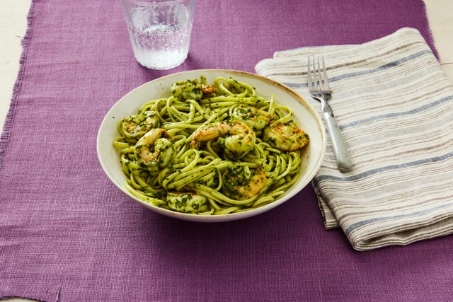 shrimp pasta with pesto on a plate with a striped napkin and a glass of water