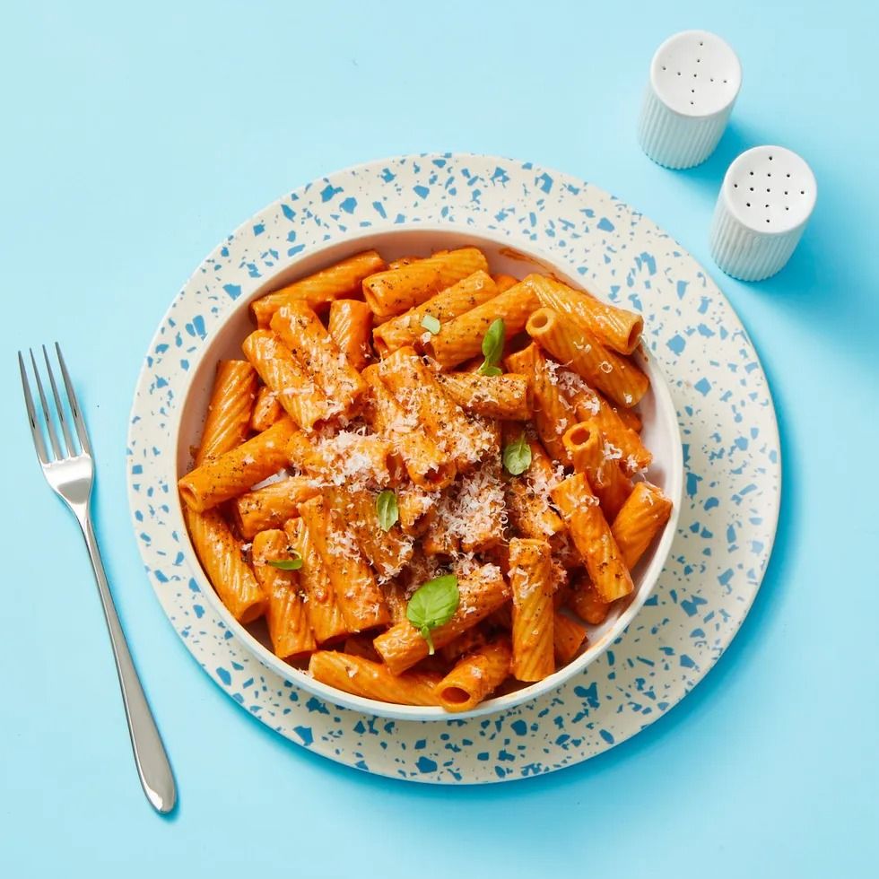 a white bowl of rigatoni with vodka sauce on a blue and white speckled plate with a fork and salt and pepper shakers
