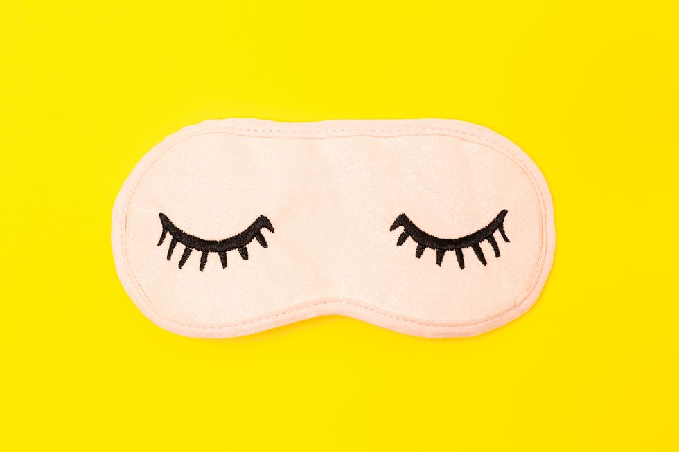 pastel pink sleep mask with closed eyes embroidered on it with eyelashes on bright yellow neon paper background top view, flat lay concept of vivid dreams