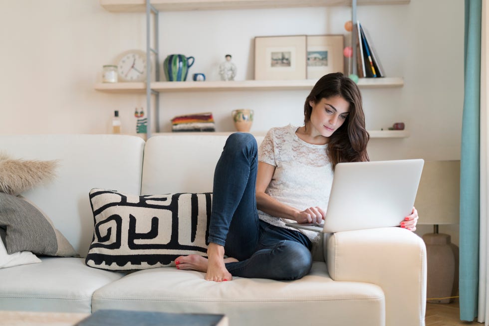 Woman sitting on couch at home using laptop