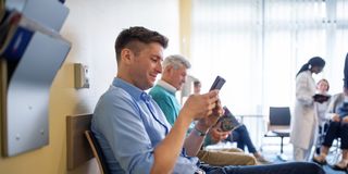patients sitting in waiting room using mobile phone