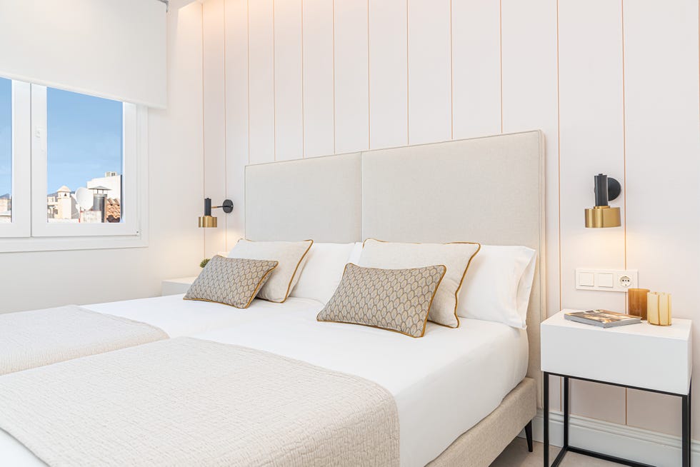 dormitorio con dos camas con cabeceros beige y papel pintado a rayas