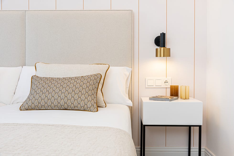 dormitorio con dos camas con cabeceros beige, mesita de noche blanca con estructura de metal negro y papel pintado a rayas