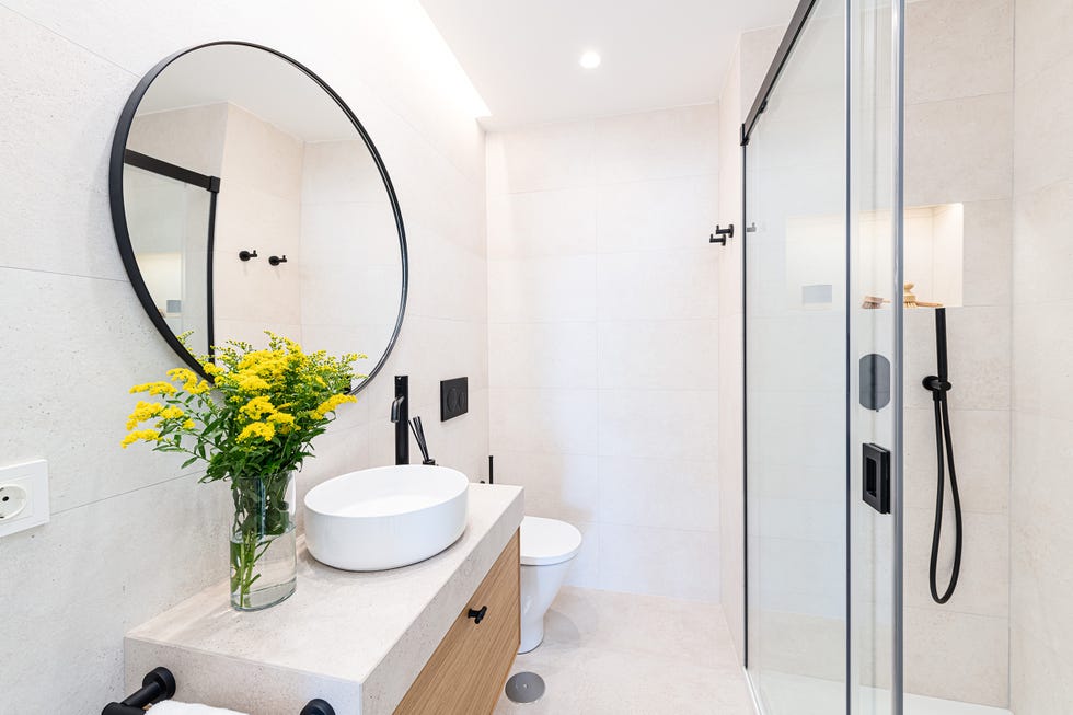 baño con ducha con perfilería negra, mueble volado y espejo redondo