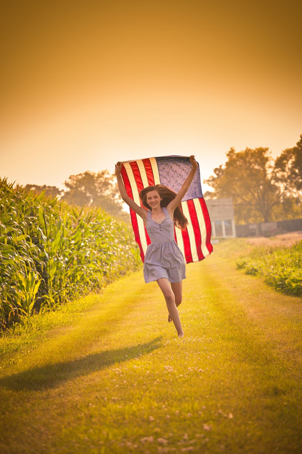 teen farm girl running through field waving us flag
