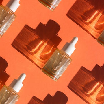 Pattern made with Glass bottle with cosmetic liquid on bright orange background with shadow and light reflections. Flat lay style and close-up pattern made with glass bottle with cosmetic liquid on bright orange background with shadow and light reflections flat lay style and close up
